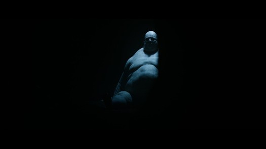 A very large, fat naked dude in shadows.