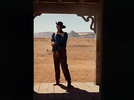 John Wayne in doorway, holding arm.